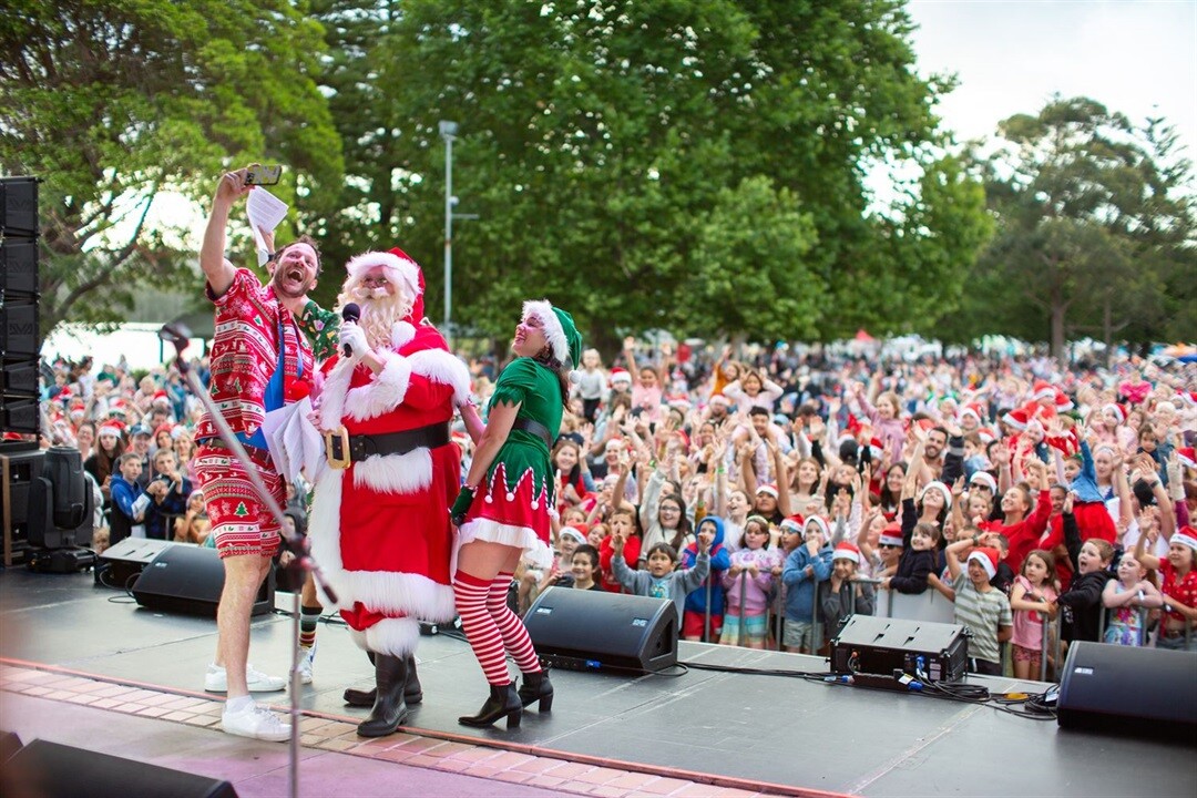 hosts-nick-jess-ducko-and-santa-take-a-selfie-in-front-of-the-lake-mac-carols-crowd